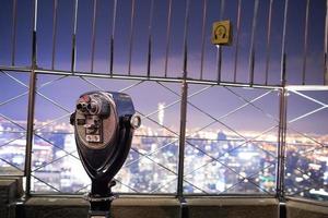 Binocolo sulla sommità dell'Empire State Building di notte a Manhattan, New York foto