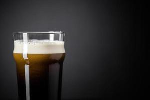 progetto di pinta di birra scura nera fresca e cremosa di azoto su sfondo nero foto