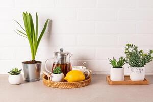 bellissimo cucina sfondo con bicchiere teiera di fragrante Tè, tazza, Limone su di vimini vassoio. davanti Visualizza. bianca mattone parete. un' copia spazio foto