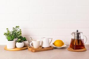 bellissimo cucina sfondo con bicchiere teiera di fragrante Tè, tazza e Limone su vassoio. davanti Visualizza. bianca mattone parete. un' copia spazio. foto