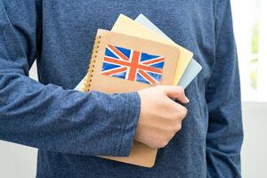 imparare inglese linguaggio, asiatico adolescenziale alunno hold libro con bandiera nel corso a scuola. foto