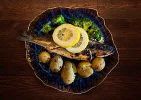 d'oro arrostito pesce con patate, Limone e broccoli, servito su di legno tavolo. sopra la testa, orizzontale - Immagine foto