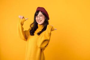 aderire il promo divertimento con un' elegante donna, indossare un' rosso berretto e giallo maglione, come lei punti sua pollice per gratuito copia spazio contro un' vivace giallo sfondo. foto