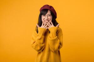 ritratto di allegro asiatico donna 30s ha timido soddisfatto espressione, sorrisi in linea di massima, indossa giallo maglione camicia e rosso berretto, pose contro giallo sfondo. etnia, emozioni foto