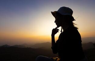 silhouette di donna seduta su montagna a tramonto foto