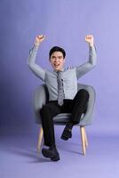 ritratto di asiatico attività commerciale uomo seduta su divano, isolato su viola sfondo foto