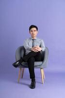 ritratto di asiatico attività commerciale uomo seduta su divano, isolato su viola sfondo foto