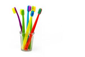 tre spazzolini da denti - viola, arancia e giallo con diverso colorato setole nel un' chiaro tazza su un' bianca sfondo. isolato. verticale. foto nel alto qualità.