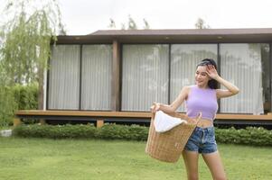 giovane asiatico donna Tenere lavanderia cestino nel Giardino dietro la casa all'aperto foto