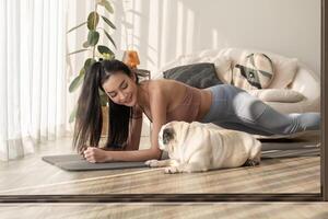 asiatico donna nel abbigliamento sportivo esercizio e fare yoga con carino cane nel vivente camera a casa, salutare stile di vita, mentale Salute concetto. foto