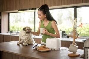 asiatico donna preparazione caffè e crostini pane per prima colazione godere con cane a il cucina tavolo nel il mattina foto