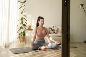 asiatico donna nel abbigliamento sportivo esercizio e fare yoga nel vivente camera a casa, salutare stile di vita, mentale Salute concetto. foto