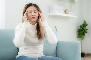 male alla testa, femmina avendo emicrania dolore, cattivo Salute, asiatico donna sensazione fatica e male alla testa, ufficio sindrome, triste stanco toccante fronte avendo emicrania o depressione, irritata ragazza, tristezza dolore foto