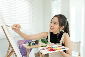 bellissimo femmina Hobby di artista e uso pennello nel astratto arte per creare capolavoro. pittore dipingere con acquerelli o olio nel studio Casa. godere pittura come passatempo, ricreazione, ispirazione foto