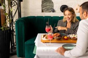 giovane coppiautilizzando mobile Telefono mentre avendo pranzo e potabile fresco spremuto succo nel il ristorante foto