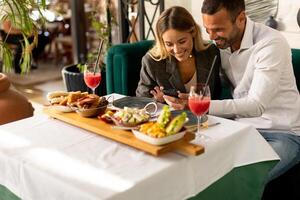 giovane coppiautilizzando mobile Telefono mentre avendo pranzo e potabile fresco spremuto succo nel il ristorante foto