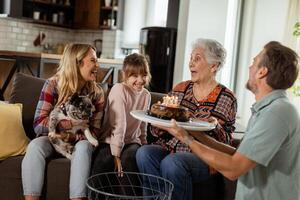 gioioso famiglia festeggiare nonne compleanno con torta nel un' accogliente vivente camera foto