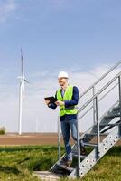 sorridente ingegnere con tavoletta ispezionando vento turbine su un' soleggiato giorno foto