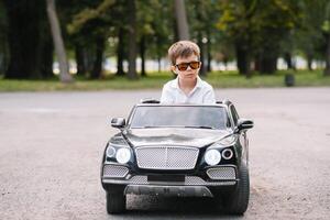 carino ragazzo nel equitazione un' nero elettrico auto nel il parco. divertente ragazzo cavalcate su un' giocattolo elettrico macchina. copia spazio. foto