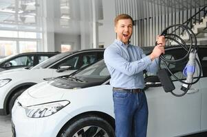 concetto di acquisto elettrico veicolo. bello attività commerciale uomo sta vicino elettrico auto a concessionaria foto