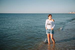 bellissimo ragazza con bella gambe a piedi lungo il riva del mare nel il estate caldo giorno vicino il mare. foto