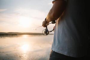 il del pescatore mani, detiene il Filatura asta, ruota il bobina maneggiare. passatempo e attività. foto