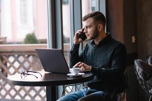 giovane uomo d'affari parlando su mobile Telefono mentre Lavorando su il computer portatile nel bar. foto