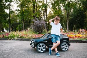 carino ragazzo nel equitazione un' nero elettrico auto nel il parco. divertente ragazzo cavalcate su un' giocattolo elettrico macchina. copia spazio. foto