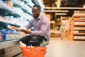 giovane africano uomo acquisto nel drogheria sezione a supermercato foto