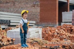 architetto nel casco scrittura qualcosa vicino nuovo costruzione. poco carino ragazzo su il edificio come un architetto foto