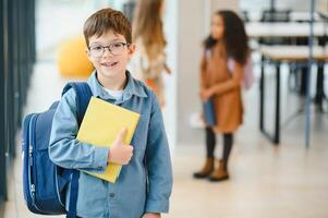 contento carino intelligente ragazzo nel bicchieri con scuola Borsa e libro nel il suo mano foto