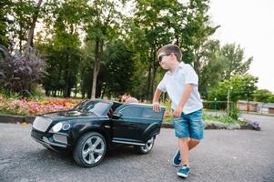 carino ragazzo nel equitazione un' nero elettrico auto nel il parco. divertente ragazzo cavalcate su un' giocattolo elettrico macchina. copia spazio. foto