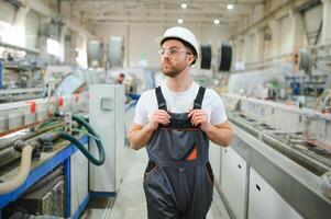 sorridente e contento dipendente. industriale lavoratore in casa nel fabbrica. giovane tecnico con difficile cappello foto