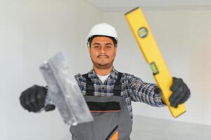 professione, costruzione e edificio - contento sorridente indiano lavoratore o costruttore nel casco al di sopra di grigio sfondo. foto