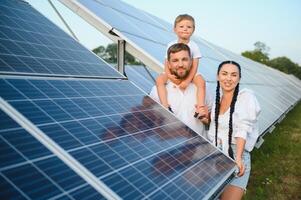 giovane famiglia di tre è accovacciato vicino fotovoltaico solare pannello, poco ragazzo e genitori. moderno famiglia concetto. il concetto di verde energia foto