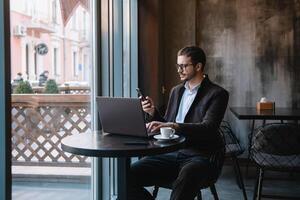 giovane uomo d'affari parlando su mobile Telefono mentre Lavorando su il computer portatile nel bar. foto