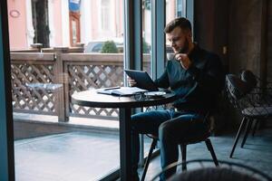 bello uomo d'affari utilizzando un' digitale tavoletta e potabile caffè mentre seduta nel bar nel il città centro. foto