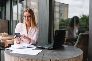 attività commerciale donna su il Telefono a ufficio. giovane attività commerciale donna avendo Telefono chiamata a il ufficio. sorridente attività commerciale donna. bella giovane attività commerciale utilizzando smartphone a il soffitta ufficio foto