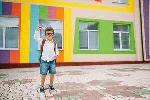 indietro per scuola. contento sorridente ragazzo nel bicchieri è andando per scuola per il primo volta. bambino con zaino e libro all'aperto. inizio di Lezioni. primo giorno di autunno foto