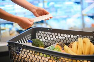 donna a supermercato Tenere un' pieno shopping carrello e un' shopping elenco foto