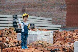 architetto nel casco scrittura qualcosa vicino nuovo costruzione. poco carino ragazzo su il edificio come un architetto foto