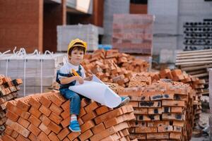 architetto nel casco scrittura qualcosa vicino nuovo costruzione. poco carino ragazzo su il edificio come un architetto foto