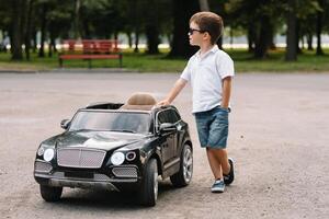 carino ragazzo nel equitazione un' nero elettrico auto nel il parco. divertente ragazzo cavalcate su un' giocattolo elettrico macchina. copia spazio. foto