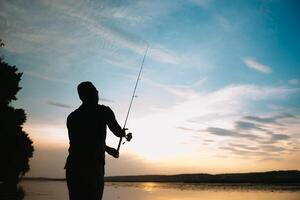 pescatore uomo pesca con Filatura asta su un' fiume banca a nebbioso nebbioso Alba. pescatore con Filatura. Filatura concetto. foto