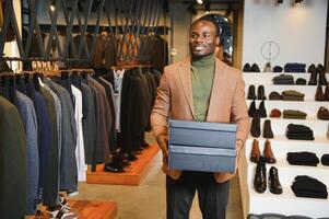 gioioso africano americano uomo trasporto shopping borse nel capi di abbigliamento negozio. moda boutique foto