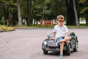 carino ragazzo nel equitazione un' nero elettrico auto nel il parco. divertente ragazzo cavalcate su un' giocattolo elettrico macchina. copia spazio. foto