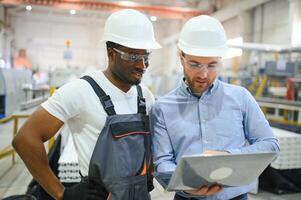 Due lavoratori nel produzione pianta come squadra discutere, industriale scena nel sfondo foto