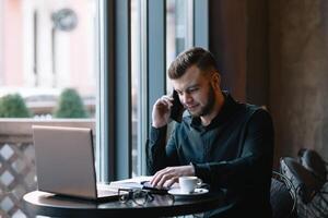 giovane uomo d'affari parlando su mobile Telefono mentre Lavorando su il computer portatile nel bar. foto