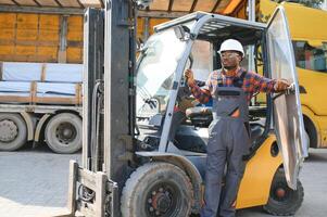 ritratto di un' contento africano americano maschio lavoratore guida carrello elevatore a forca a posto di lavoro foto