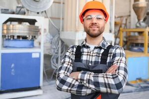 sorridente e contento dipendente. industriale lavoratore in casa nel fabbrica. giovane tecnico con difficile cappello foto